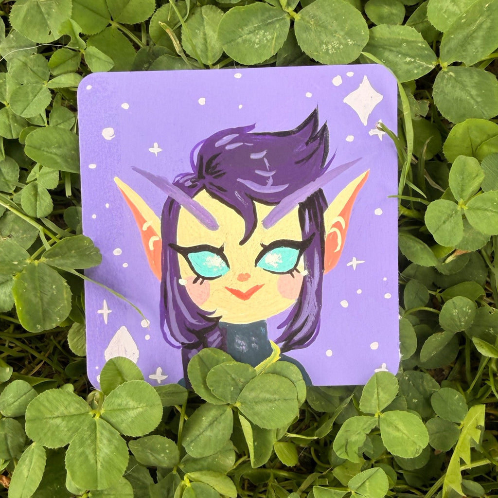 A square art print featuring a stylized purple-haired character on a lavender background, placed on green clover outdoors.